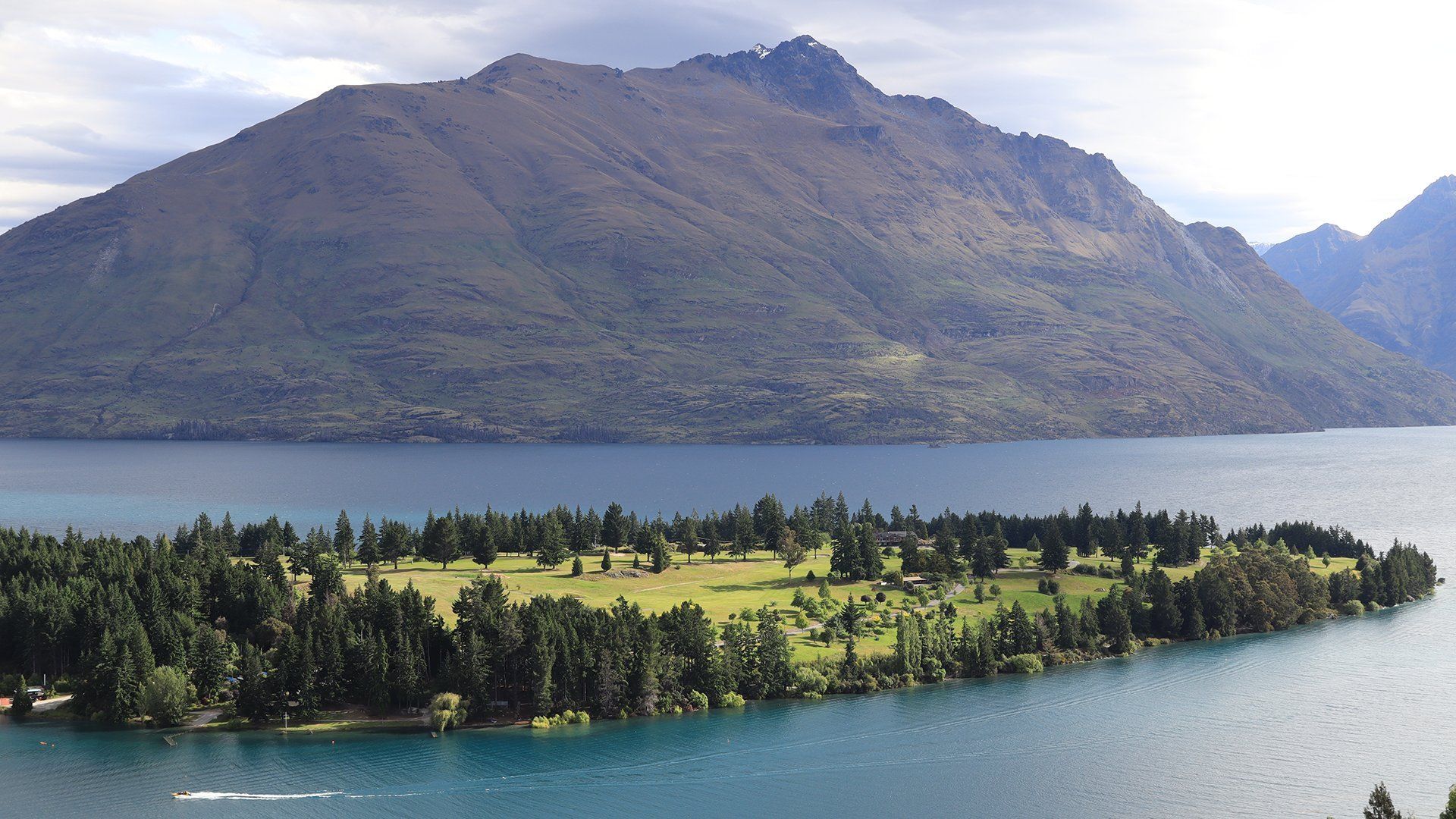 Mountains in New Zealand with a boat cruising along the lake