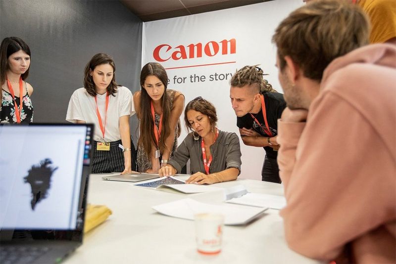 Students stand around a table looking at a photograph.