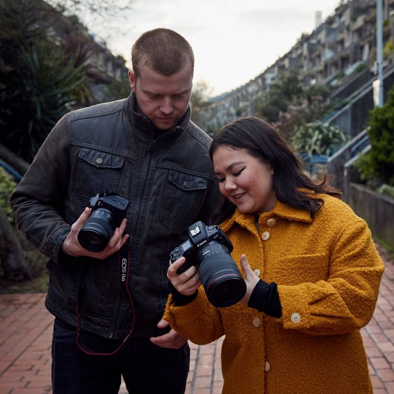 Two people leaning in to look at the back of a Canon camera.