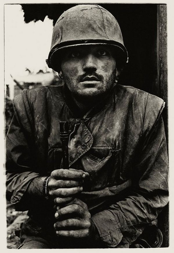 A shell-shocked US Marine gazes at the camera, dressed in army fatigues and clutching his rifle between his hands, in Sir Don McCullin's iconic shot of the Vietnam War.