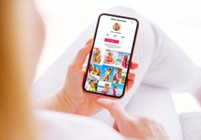 A pair of hands holds a phone displaying a TikTok profile screen.