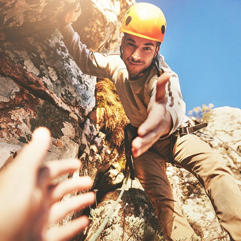 Rock climbing man leans down to take someone's hand