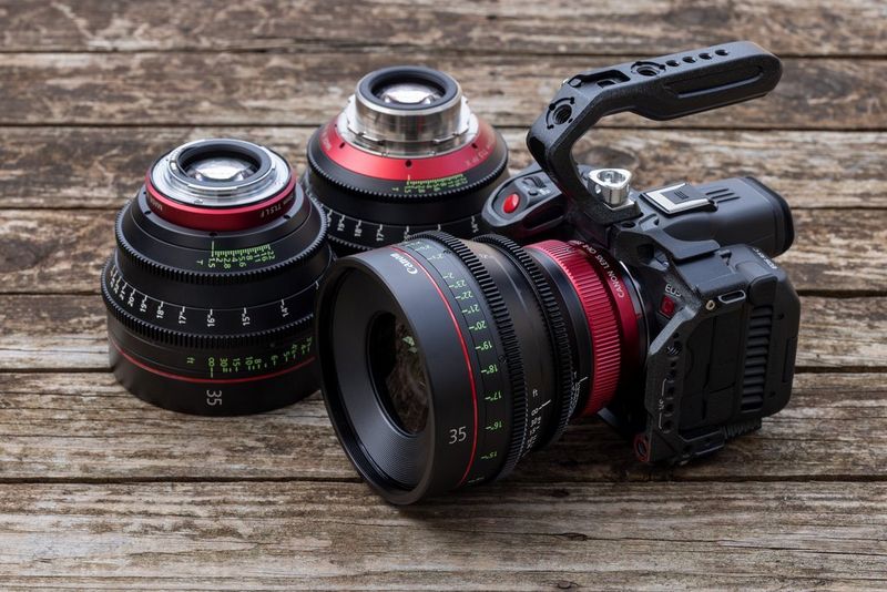 Eine Canon EOS R5 C, an der eine CN-R Festbrennweite befestigt ist, liegt auf einer Holzoberfläche neben einer CN-E Festbrennweite (links) und einer Sumire Festbrennweite.