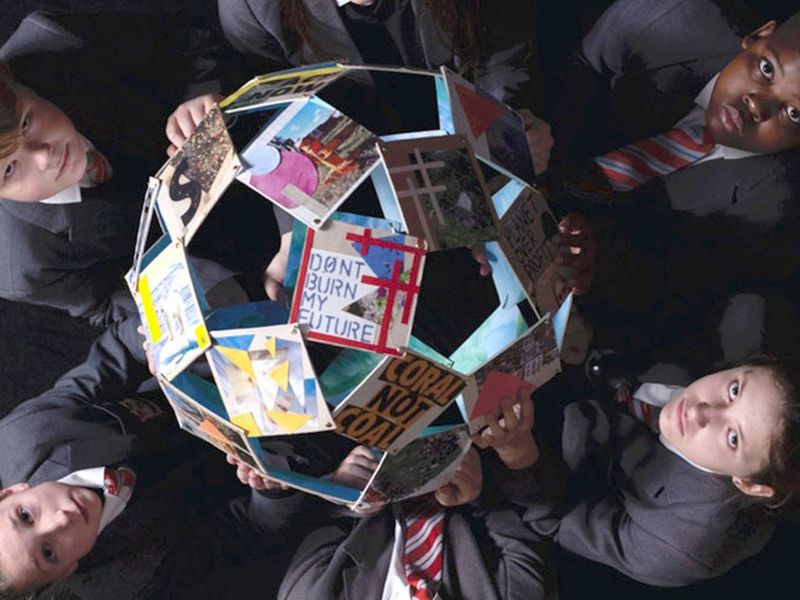 Taken from above, two children, on the left and right of the photo, hold a globe made of photographs and raise their solemn faces to the camera. The clearest photo, closest to the camera displays the words dont burn my future.