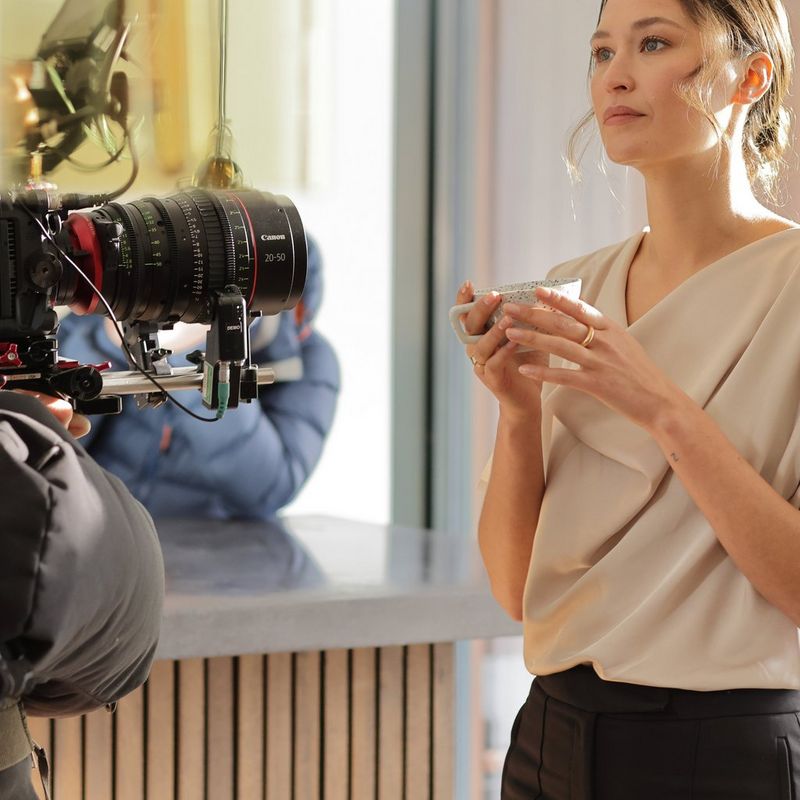 A woman holding a cup being filmed by a Canon Cinema EOS camera with a Canon Flex Zoom lens attached.
