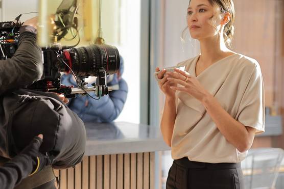 A woman holding a cup being filmed by a Canon Cinema EOS camera with a Canon Flex Zoom lens attached.
