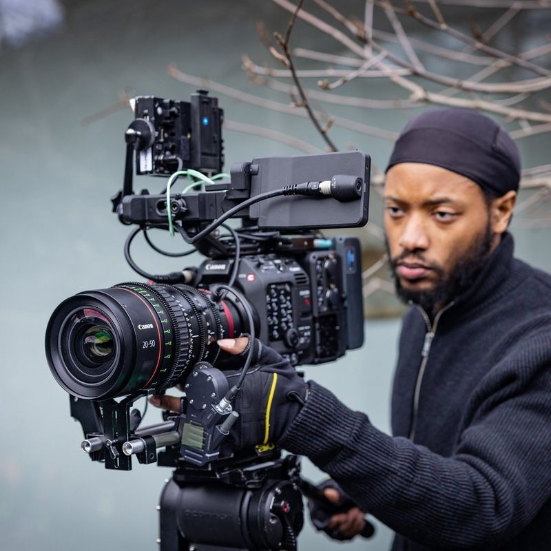 A filmmaker stands behind a Canon Cinema EOS camera with a Canon Flex Zoom lens attached.