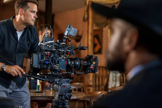  A man adjusts a large camera rig on the set of an old-fashioned Western bar.