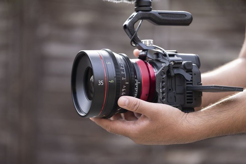 A pair of hands holds a Canon EOS R5 C camera with Canon 35mm prime lens attached.