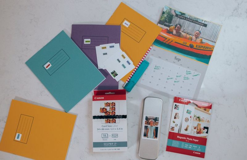 A top-down image of a selection of colourful exercise books, a calendar, stickers and Canon printer paper.