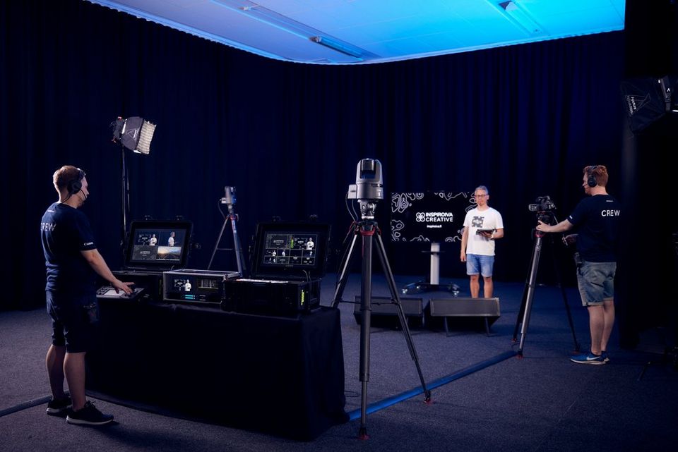 A studio scene with several different cameras including Canon PTZ cameras on tripods and an operator at a control desk using a Canon RC-IP100 hardware controller.