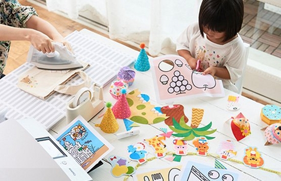A child sat at a table with a parent creating colourful papercrafts using a Canon printer.