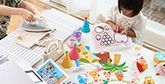 A table filled with paper craft items and a child making them under adult supervision.