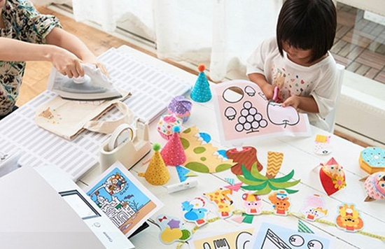 A table filled with paper craft items and a child making them under adult supervision.