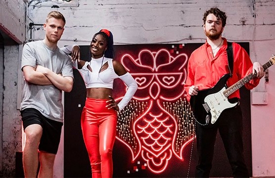 A musician, a dancer and a footballer standing in front of a wall with a neon graffitied owl on it.