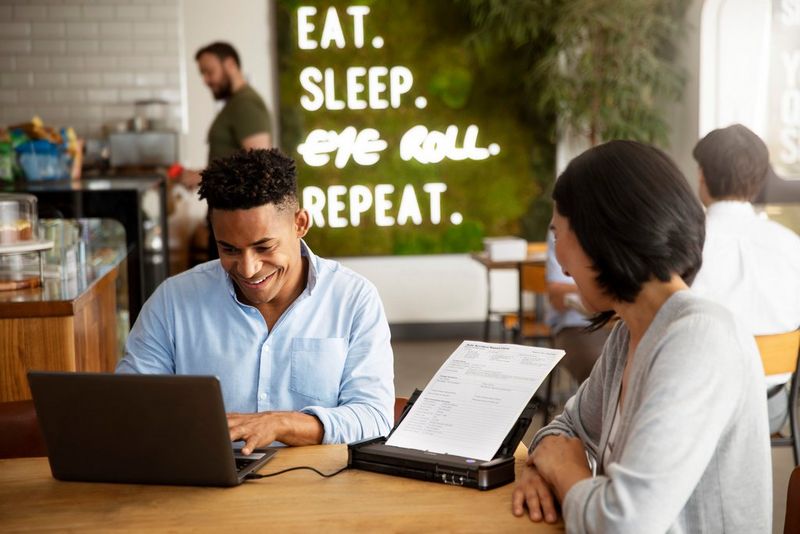 People collaborating over a document scanner in a coffee shop – Canon UK