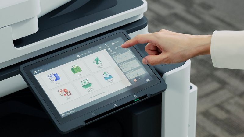 A hand using the touchscreen control panel of the Canon imageFORCE C7165 multifunction printer.