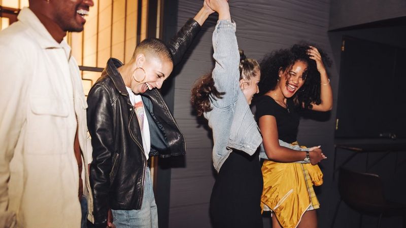 An unposed shot of four young people on a night out. They are holding hands and laughing hard.