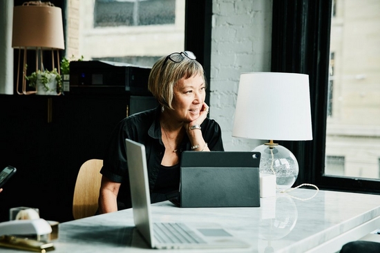 Woman sits with her iPad on a marble table, looking out the window