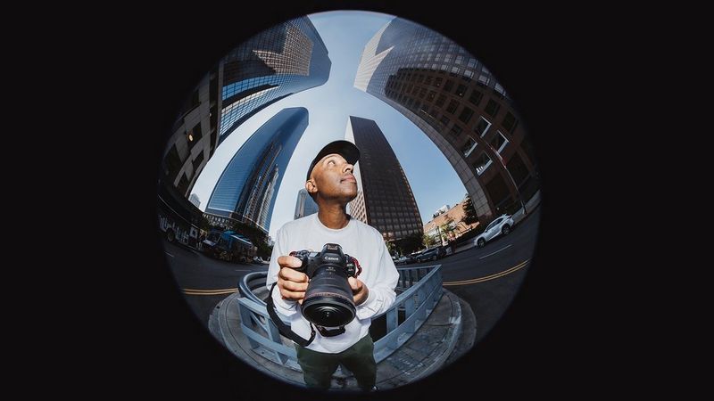 Photo fisheye d'une personne tenant un appareil photo Canon au milieu de grands bâtiments urbains