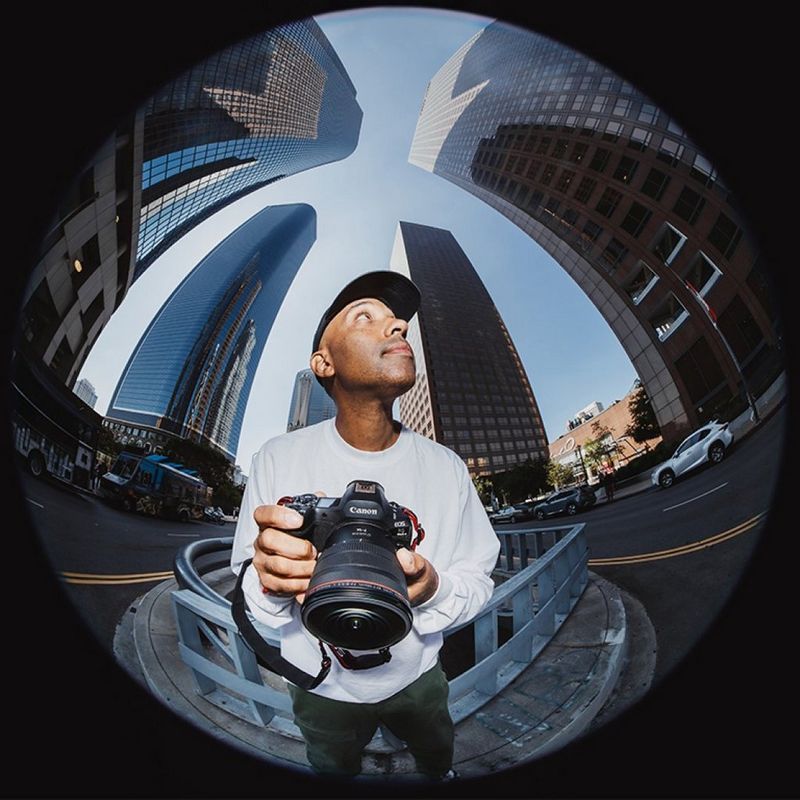 Photo fisheye d'une personne tenant un appareil photo Canon au milieu de grands bâtiments urbains
