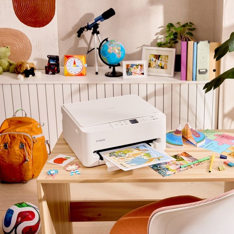 Een Canon-printer op het bureau van een kind, print een kleurrijk vel, met schoolspullen, foto’s en speelgoed eromheen.