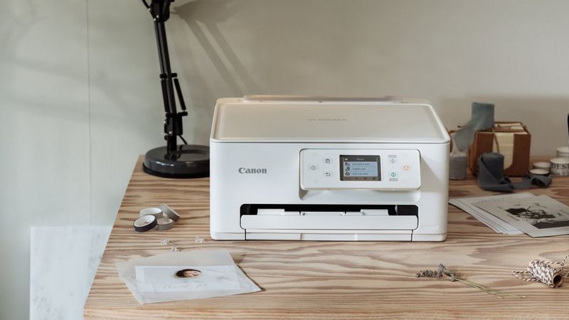 Canon Drucker auf einem Holztisch mit Fotodrucken, Bastelzubehör und einer Schreibtischlampe in einem kreativen Arbeitsbereich.