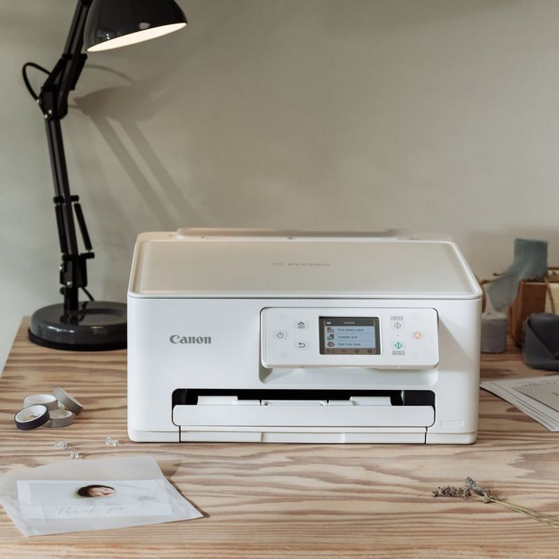 Imprimante Canon sur un bureau en bois avec des tirages photo, des fournitures de création et une lampe de bureau dans un espace de travail créatif.