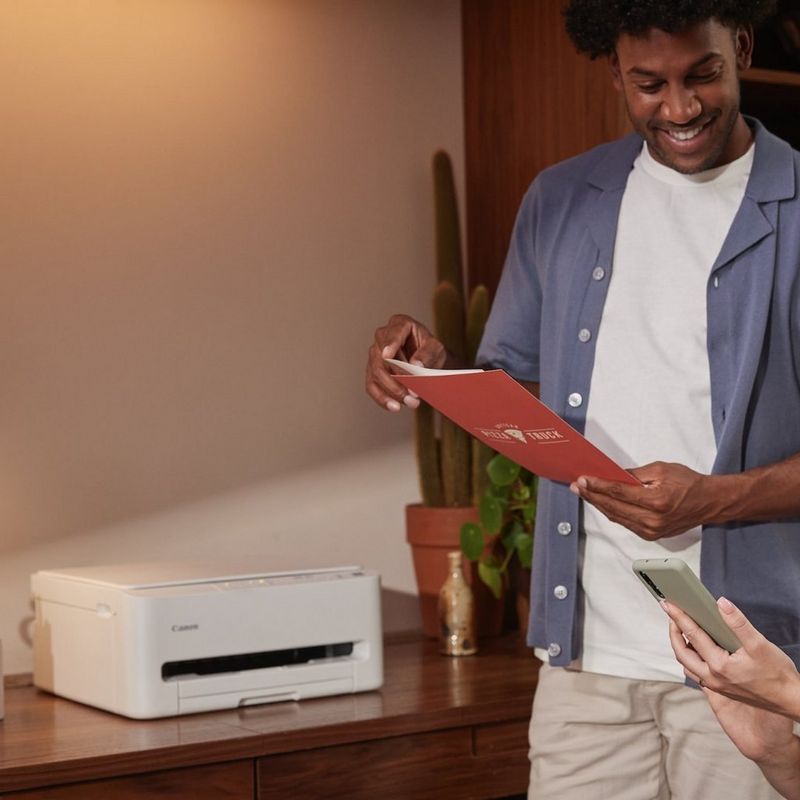 Two people using a Canon printer on a wooden desk in a warmly lit room