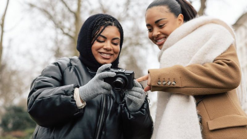 Two people looking at a Canon PowerShot V1 outdoors, with one person pointing at the screen