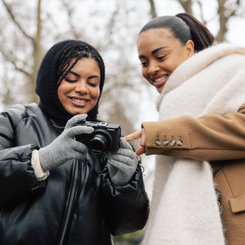 Two people looking at a Canon PowerShot V1 outdoors, with one person pointing at the screen