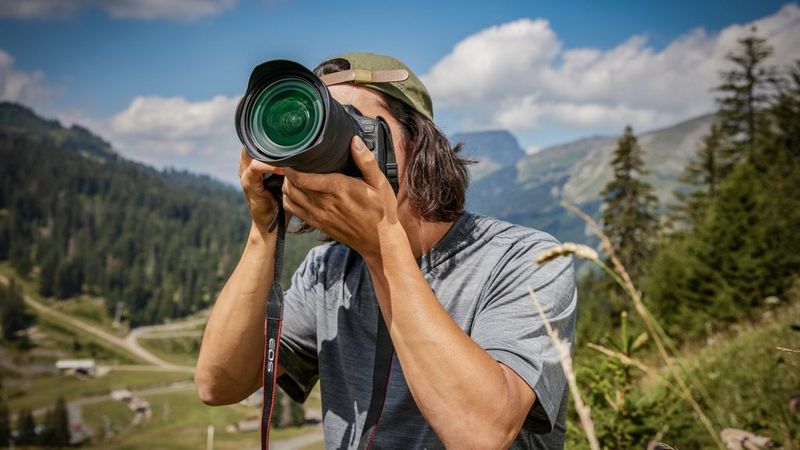 Profissional de fotografia a utilizar uma câmara Canon com uma objetiva grande para fotografar uma paisagem montanhosa ao ar livre