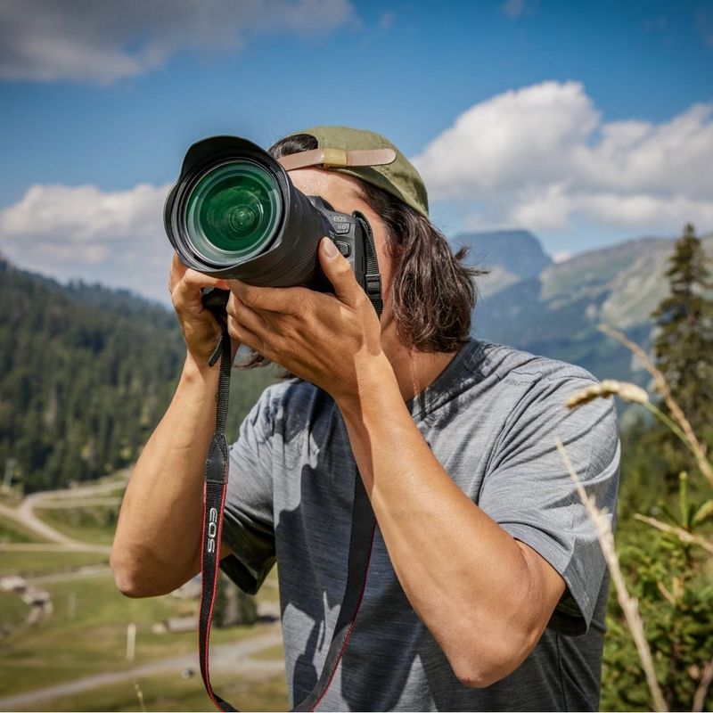 Un fotógrafo utiliza una cámara Canon con un objetivo grande para fotografiar un paisaje montañoso al aire libre