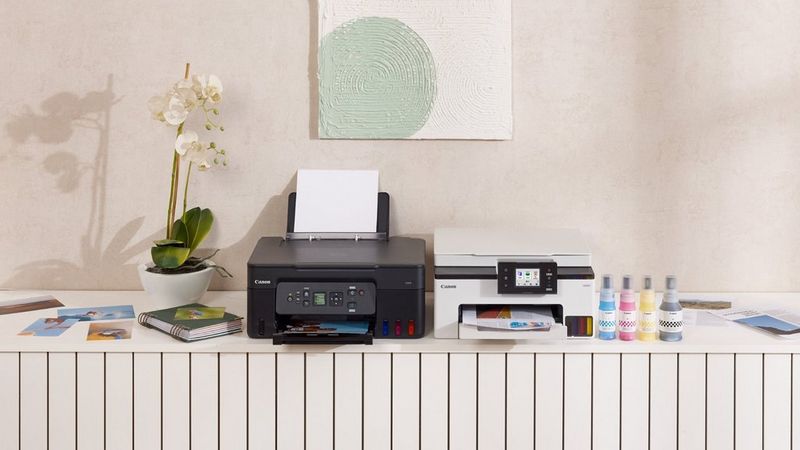 Canon MegaTank printers on a white cabinet next to ink bottles, an orchid and wall art