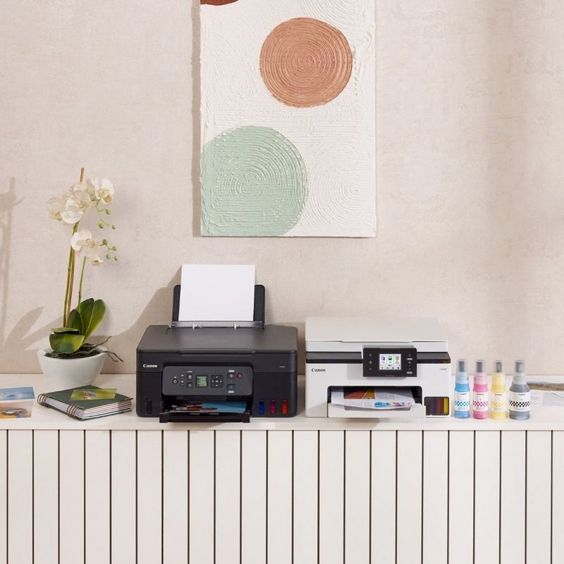 Canon MegaTank printers on a white cabinet next to ink bottles, an orchid and wall art