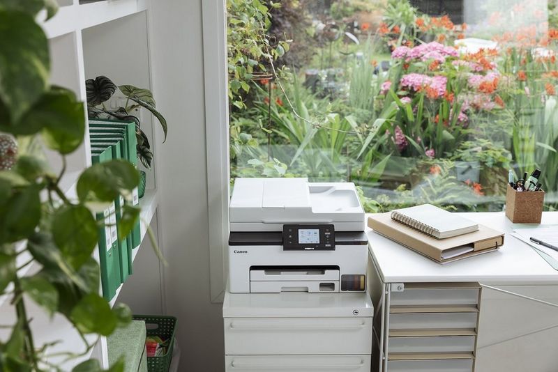 Imprimante Canon dans un espace de travail à la maison, à côté d'une fenêtre surplombant un jardin rempli de fleurs et de verdure