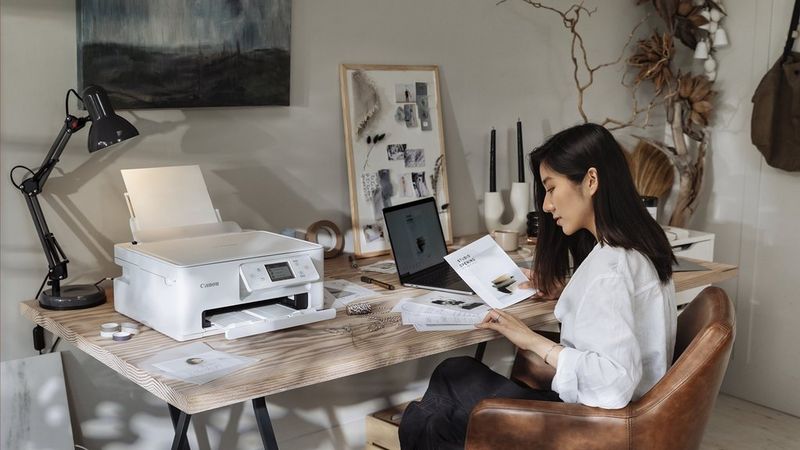 PIXMA-printer på en hjemmearbejdsplads med en person, der bruger en bærbar computer til at printe dokumenter.