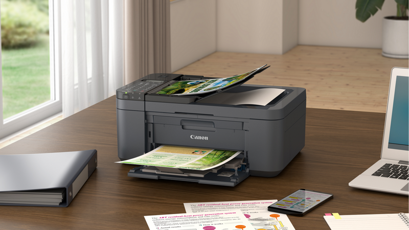 PIXMA TR-seriens printer på et skrivebord med printede fotos, kontorartikler og en bærbar computer på et hjemmekontor.