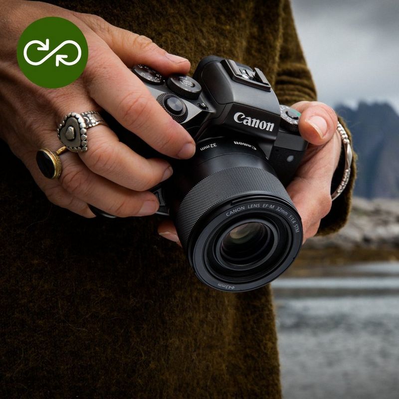 Pessoa a segurar uma câmara mirrorless Canon junto a um lago, com montanhas ao fundo