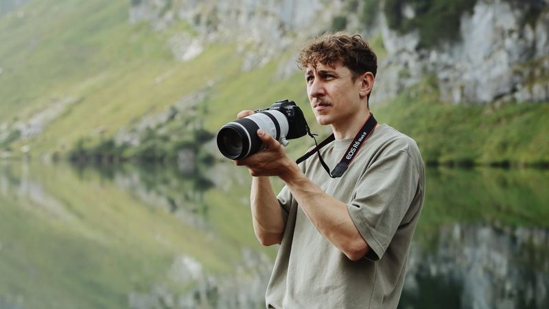 Fotografo che utilizza una fotocamera Canon con teleobiettivo accanto a un lago tranquillo e a un pendio roccioso