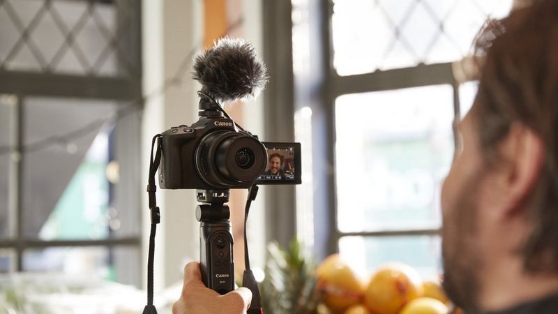 A man filming himself, holding a Canon camera with the screen flipped towards him