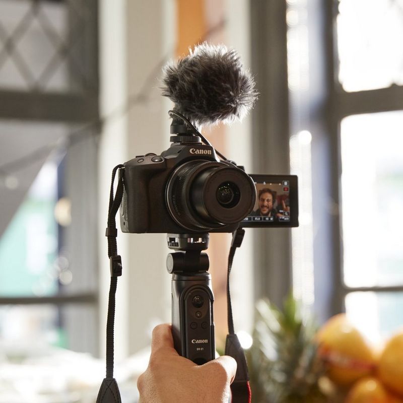 A man filming himself, holding a Canon camera with the screen flipped towards him