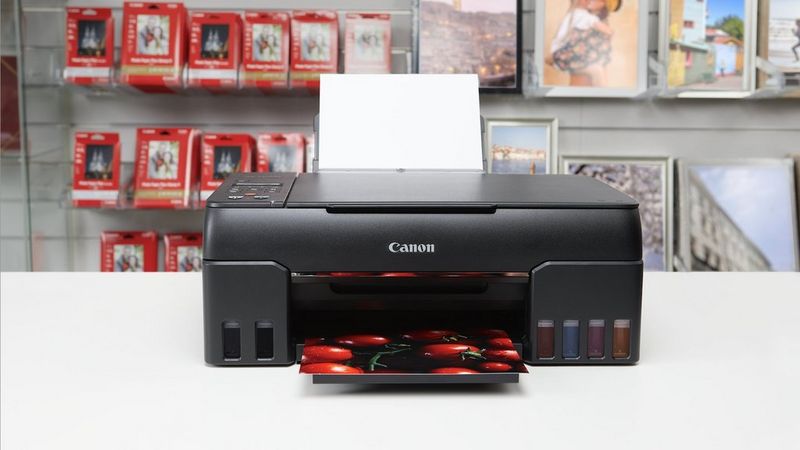 Canon PIXMA G650 printer printing a photo in a retail setting with Canon paper packs behind.