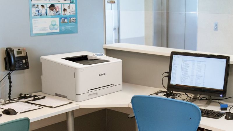 Canon i-SENSYS LBP647Cdw printer on an office desk beside a computer monitor.