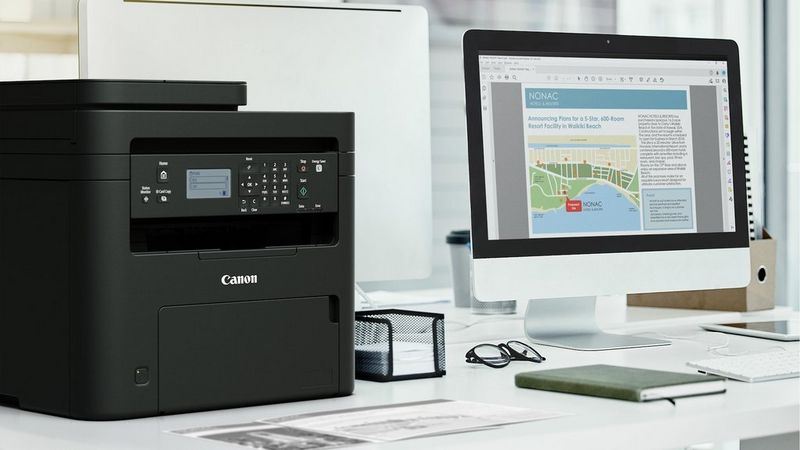Canon i-SENSYS MF272dw printer on a desk beside a computer in a home office workspace.