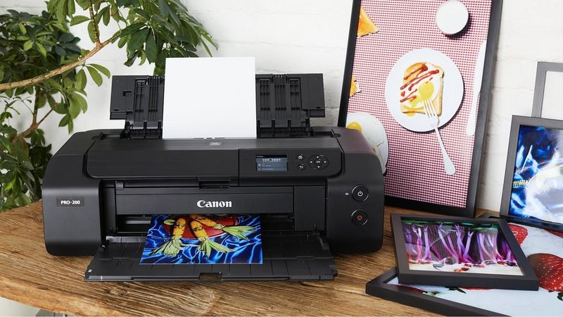 Canon PIXMA PRO-200S printer printing colourful artwork beside framed prints and a tablet.