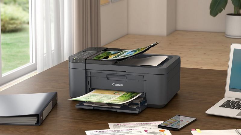 Canon PIXMA TR4755i printer on a home office desk printing documents beside a laptop.