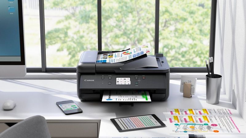 Canon PIXMA TR7650 printer on a home office desk printing documents beside stationery and charts.