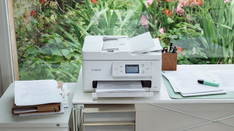 Canon PIXMA TR7650 printer on a home office desk printing documents beside stationery and charts.