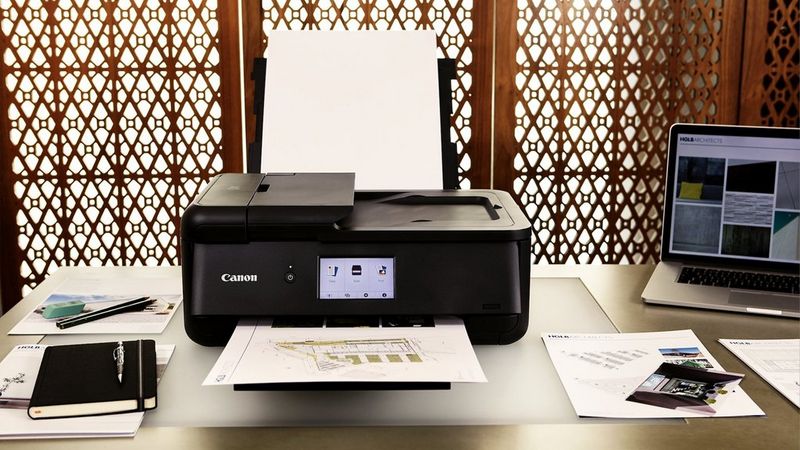 Canon PIXMA TS9550a printer on a desk printing a document beside a laptop and stationery